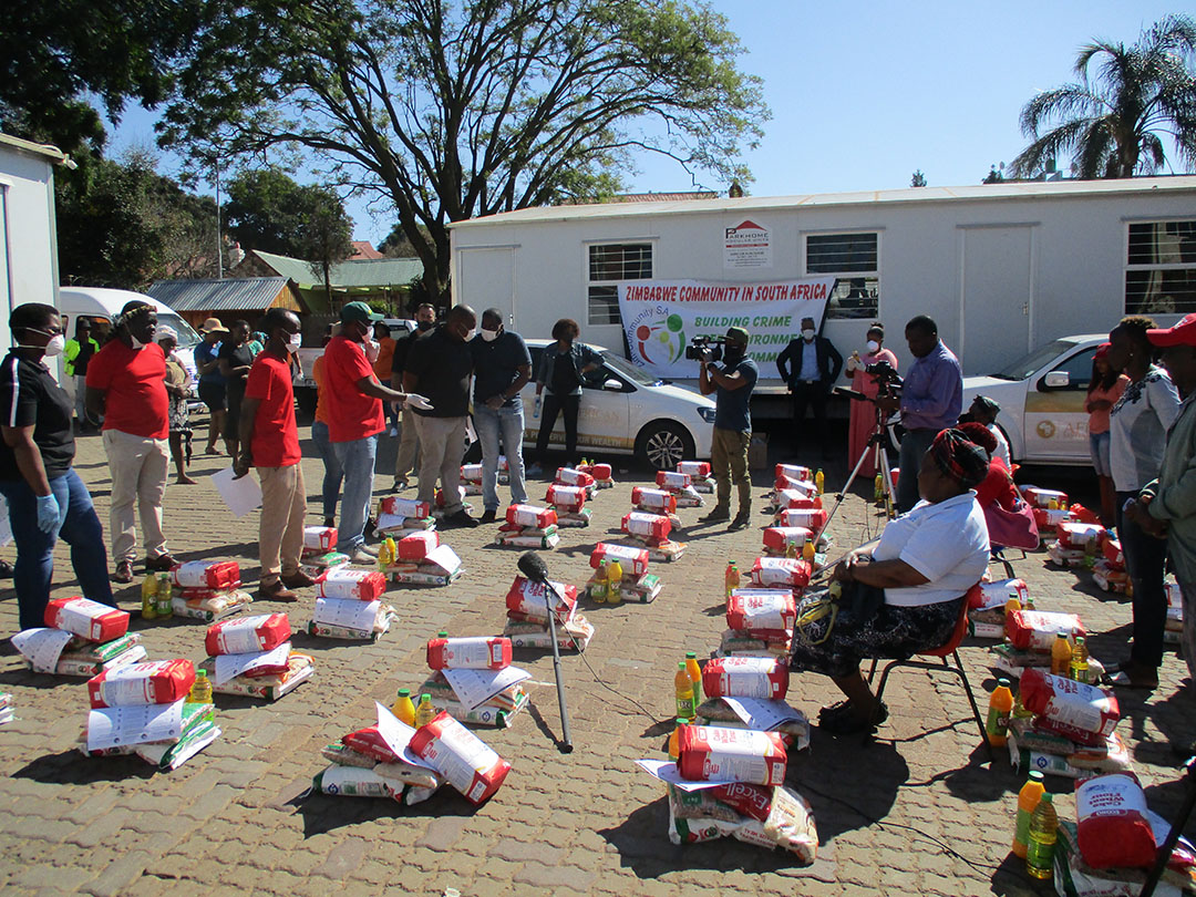 People gathered outdoors around arranged food packages at a community event.